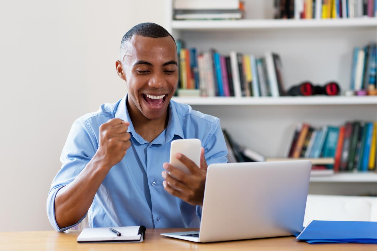 Smiling man using phone while working on computer